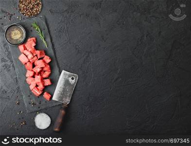 Raw lean diced casserole beef pork steak on chopping board with vintage meat hatchet on stone background. Salt and pepper