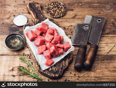 Raw lean diced casserole beef pork steak on chopping board with vintage meat hatchets on wooden background. Salt and pepper