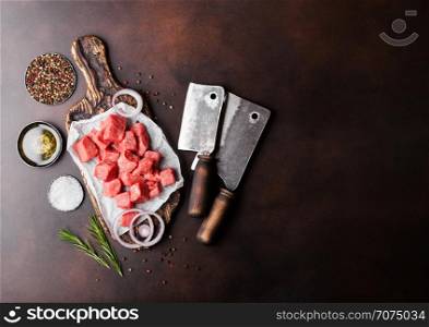 Raw lean diced casserole beef pork steak on chopping board with vintage meat hatchets on brown background. Salt and pepper