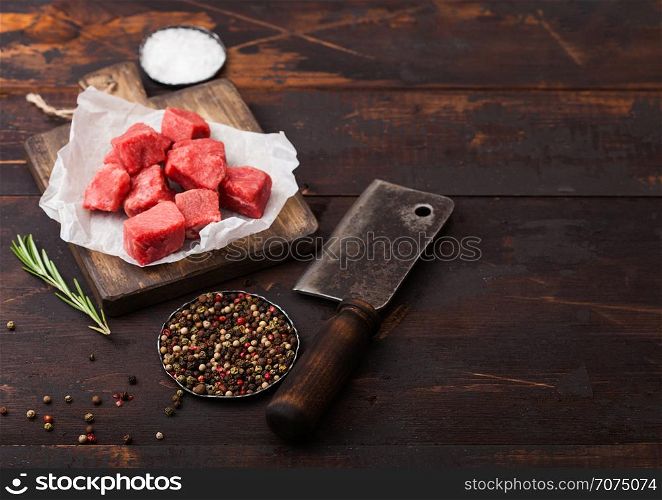 Raw lean diced casserole beef pork steak on chopping board with vintage meat hatchet on wooden background. Salt and pepper