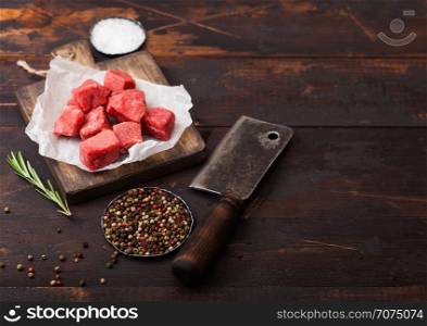 Raw lean diced casserole beef pork steak on chopping board with vintage meat hatchet on wooden background. Salt and pepper