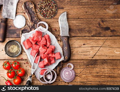 Raw lean diced casserole beef pork steak with vintage meat hatchet and knife on wooden background. Salt and pepper with fresh rosemary, red onion and garlic.