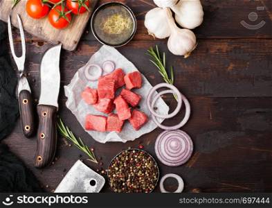 Raw lean diced casserole beef pork steak with vintage meat hatchet and knife and fork on wooden background. Salt and pepper with fresh rosemary, red onion and garlic.