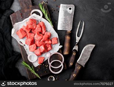 Raw lean diced casserole beef pork steak with vintage meat hatchet and fork with knife on stone background. Rosemary with red onion.