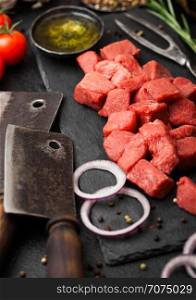 Raw lean diced casserole beef pork steak with vintage meat hatchet and fork on stone background. Salt and pepper with fresh rosemary, red onion and garlic.