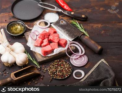 Raw lean diced casserole beef pork steak with vintage meat hatchet and fork on wooden background. Salt and pepper with fresh rosemary, red onion and garlic.