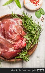raw leg of lamb in wooden plate with rosemary and peppercorn on rustic background, close up
