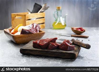 Raw liver and vegetables on textured concrete gray background. Ingredients for cooking pate or liver pancakes  tomatoes, onions, garlic and spices. Top view, space for text. Raw liver and vegetables on textured concrete gray background.