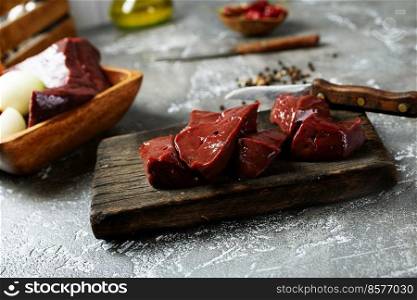 Raw liver and vegetables on textured concrete gray background. Ingredients for cooking pate or liver pancakes: tomatoes, onions, garlic and spices. Top view, space for text. Raw liver and vegetables on textured concrete gray background.