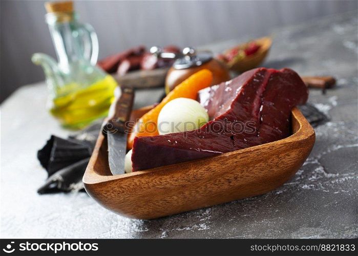 Raw liver on slate board on wooden background top view