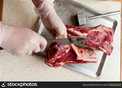 raw marbled beef edge on an aluminum tray and gloved hands with knife