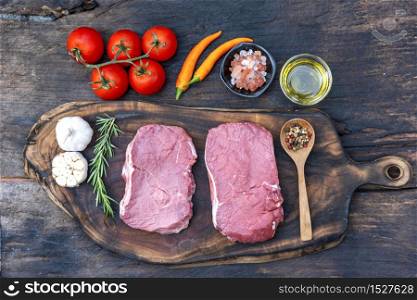 Raw meat beef steak organic fresh ingredient on wooden board table background in kitchen with rosemary, salt, garlic, tomato, black pepper, olive oil. Meat beef on wooden plate for beefsteak raw meat