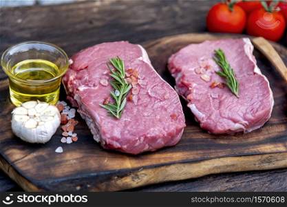 Raw meat beef steak organic fresh ingredient on wooden board table background in kitchen with rosemary, salt, garlic, tomato, black pepper, olive oil. Meat beef on wooden plate for beefsteak raw meat