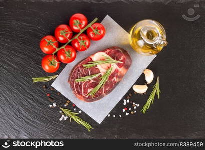 raw meat beef steak with bone, spices, rosemary and cooking ingredients on cutting board and black slate background. top view, flat lay.. raw meat beef steak with bone on paper and black slate background. top view, flat lay.