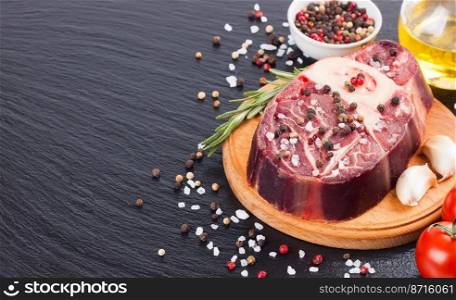 raw meat beef steak with bone, spices, rosemary and cooking ingredients on cutting board and black slate background. empty space for text.. meat steak and cooking ingredients on black background