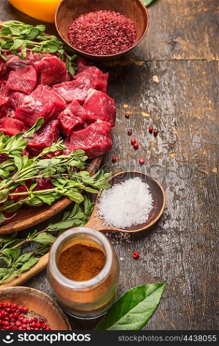 Raw meat cubes with herbs and spices. Goulash cooking preparation on rustic wooden background, place for text