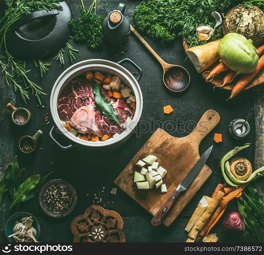 Raw meat in cooking pot on kitchen table background with vegetables , seasoning and kitchen utensils, top view. Flat lay. Meat dishes recipes. Broth, meat bone stock or soup cooking preparation