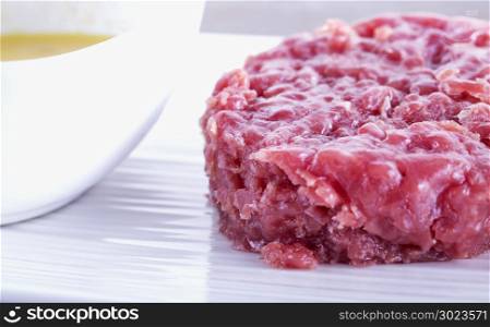 Raw meat over white plate with yellow sauce, horizontal image