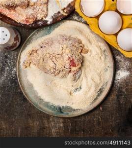 raw Meat schnitzel preparation in plate with flour, eggs and crumbs on wooden background, top view, close up