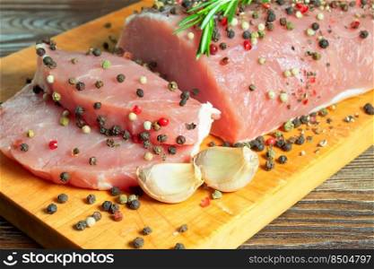 raw meat steak with spices on a cutting board. Pork, rosemary, pepper, spice and garlic on wooden background. Raw pork meat steak