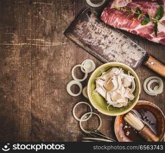 Raw meat with Butcher Cleaver and ingredients for meat grilling on rustic wooden background, top view