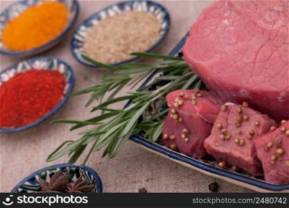raw meat with spices and herbs in a square plate on a textured tissue. raw meat with spices