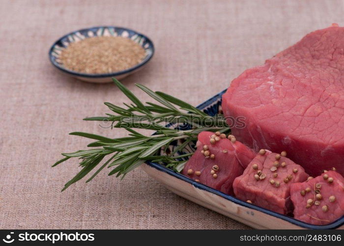 raw meat with spices and herbs in a square plate on a textured tissue. raw meat with spices