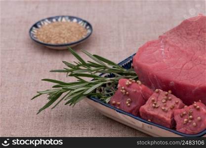 raw meat with spices and herbs in a square plate on a textured tissue. raw meat with spices