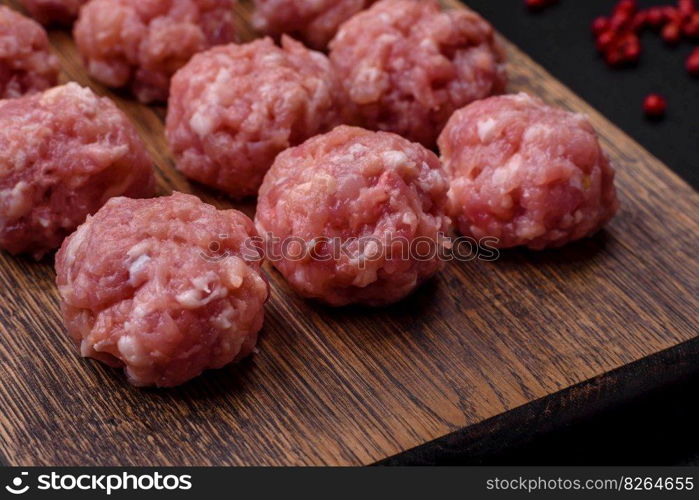 Raw meatballs of minced meat beef, pork or chicken with salt, spices and herbs on a dark concrete background