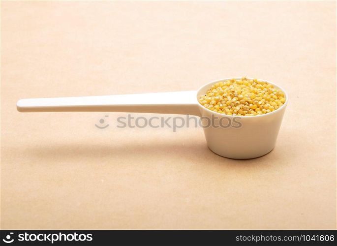 Raw millet in measuring spoon on brown background
