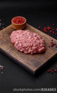 Raw minced beef, pork or chicken meat with salt, spices and herbs on a dark concrete background