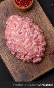 Raw minced beef, pork or chicken meat with salt, spices and herbs on a dark concrete background
