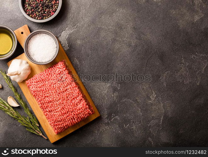 Raw minced homemade beef meat with spices and herbs. Top view. On top of chopping board and kitchen table background. With pepper salt and garlic.