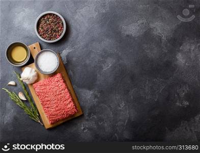 Raw minced homemade beef meat with spices and herbs. Top view. On top of chopping board and kitchen table background. With pepper salt and garlic.