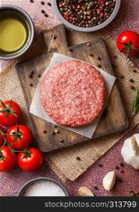 Raw minced homemade grill beef burger with spices and herbs. Top view. On top of chopping board and rusty kitchen table background. With pepper salt and garlic.