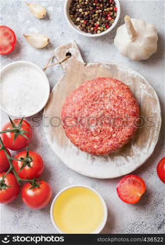 Raw minced homemade grill beef burger with spices and herbs. Top view. On top of white chopping board and kitchen table background. With pepper salt and garlic.