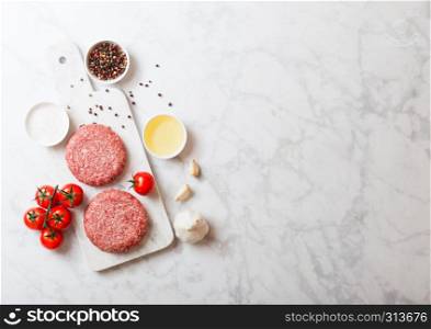 Raw minced homemade grill beef burgers with spices and herbs. Top view and space for text. On top of chopping board and marble kitchen table background. With pepper salt and oil.