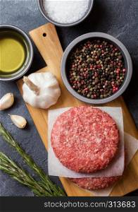 Raw minced homemade grill beef burgers with spices and herbs. Top view and space for text. On top of chopping board and kitchen table background. With pepper salt and garlic.