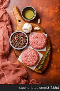 Raw minced homemade grill beef burgers with spices and herbs. Top view and space for text. On top of chopping board and rusty kitchen table background. With pepper salt and garlic.