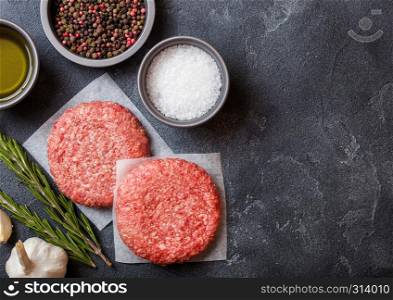 Raw minced homemade grill beef burgers with spices and herbs. Top view and space for text. Pepper, salt and oil on kitchen table background.