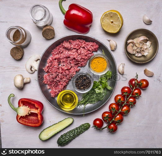 raw minced meat, half lined with pan with spices and herbs and butter, with tomatakmi on a branch, peppers, cucumbers and salt on wooden rustic background top view