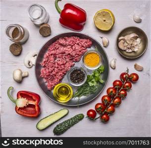 raw minced meat, half lined with pan with spices and herbs and butter, with tomatakmi on a branch, peppers, cucumbers and salt on wooden rustic background top view