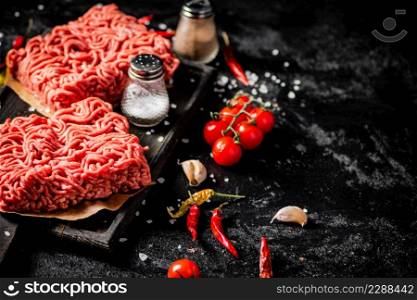 Raw minced meat on a cutting board with cherry tomatoes. On a black background. High quality photo. Raw minced meat on a cutting board with cherry tomatoes.
