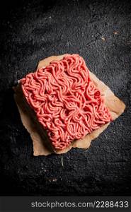 Raw minced meat on paper on the table. On a black background. High quality photo. Raw minced meat on paper on the table.