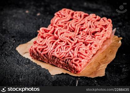 Raw minced meat on paper on the table. On a black background. High quality photo. Raw minced meat on paper on the table.
