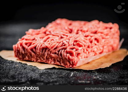 Raw minced meat on paper on the table. On a black background. High quality photo. Raw minced meat on paper on the table.