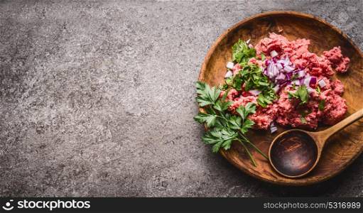 Raw minced meat stuffing in wooden bowl and spoon on gray stone background, top view, place for text. Cooking,recipes and eating concept