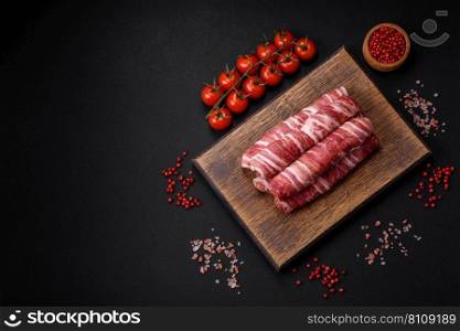Raw minced meat wrapped in bacon with salt and spices or cevapcici on a dark concrete background