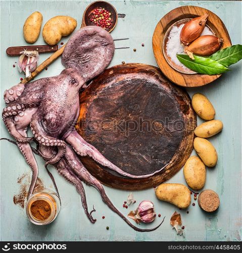 Raw octopus around empty wooden plate with ingredients for spanish cooking: potatoes and spices on rustic background, top view