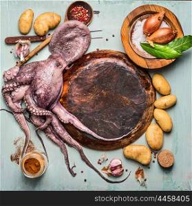 Raw octopus around empty wooden plate with ingredients for spanish cooking: potatoes and spices on rustic background, top view